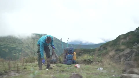 A man collects garbage and plastic in a bag in the mountains. Stock Footage 214328936