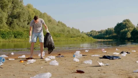 Man is collects plastic trash on polluted river and listens favorite song Stock Footage 123876407