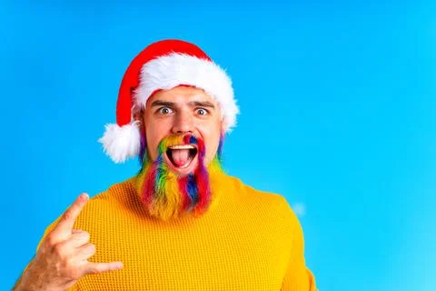 Man with colored rainbow beard in the red Santa Claus costume in blue studio Stock Photos