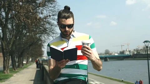 Man in colorful shirt drinking coffee on boulevards and reading book Stock Footage
