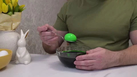 Man is coloring easter eggs at home, showing the process of dipping a white egg Stock Footage 305024168
