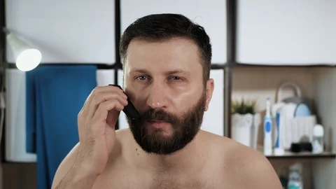 Man is combing his beard. Attractive man in bathroom looks in mirror and combes 動画素材 128228287