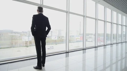 Man come and stand at full height, gaze out airport terminal window Stock Footage 82417934