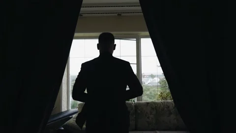 A man comes to the bright window putting on a jacket. He's going to a meeting Stock Footage 159407021