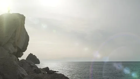 Man comes to the edge of a cliff, raises his hands to the sides and admires the Stock Footage
