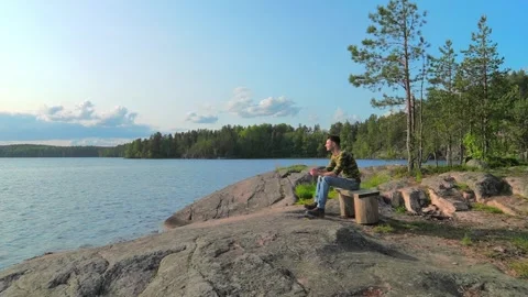 The man comes up, sits on a bench on the stone shore lake and looks. Stock Footage 311827476