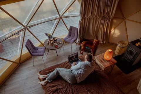 A man is comfortably lying on a bed using a laptop for content Stock Photos