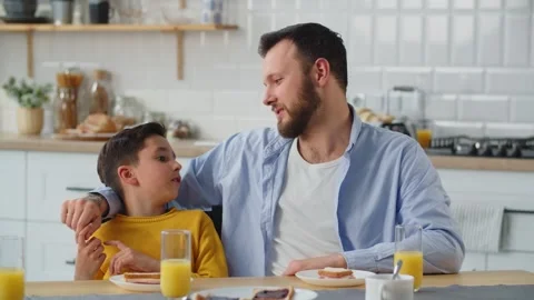 A man communicates with his son while sitting at a table in the kitchen. The Stock Footage 240194963