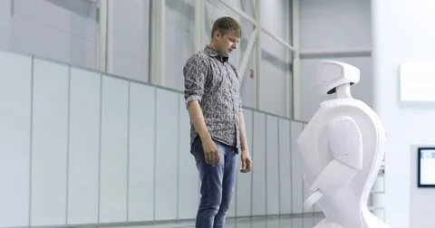 A man communicates with a robot, presses a plastic mechanical arm to the robot Stock Footage 76955871