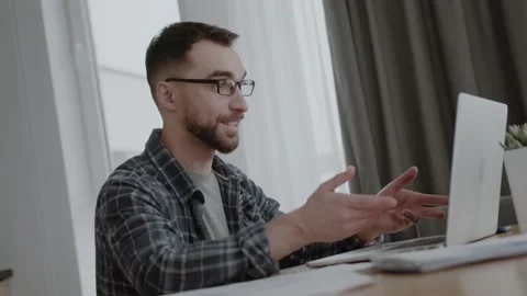 A man communicates by videoconference via a laptop. A 30s man in casual at a Stock Footage 156405927