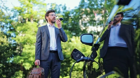 Man Communicates via Voice Assistant During Electric Vehicle Charging Moment Stock-Footage 312663442