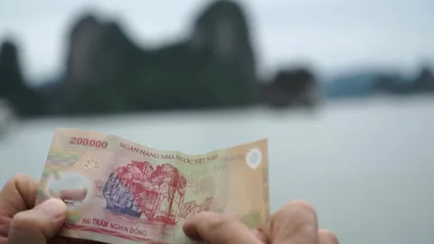 A man compares the image on a 200,000 dong banknote to a cliff in HaLong Bay 動画素材 311584649