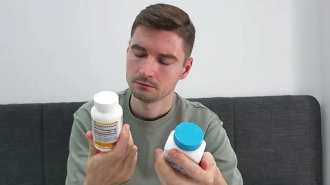 Man comparing two supplement bottles while seated on a sofa Video stock 284045058
