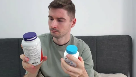 Man comparing two supplement bottles while sitting on a couch. Stock Footage 284045886