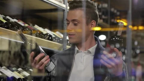 Man comparing two wine bottles with a thoughtful smile Stock Footage 311919548