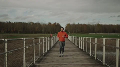 Man completes his run on a scenic bridge, checking his smartwatch for distance Stock Footage 327875299