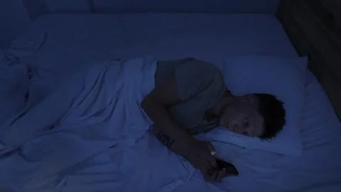 Man compulsively scrolling smartphone in bed at night, struggling with digital Stockbeeldmateriaal 346244908