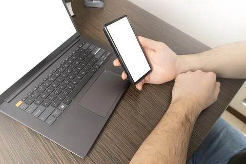 A man at a computer. Close-up of a hand, Mockup. White laptop and phone screen. Stock Photos