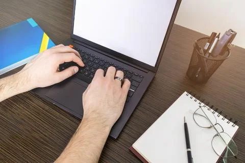 A man at a computer. Close-up of a hand, Mockup. White laptop and phone screen. Stock Photos
