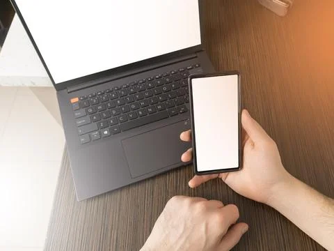 A man at a computer. Close-up of a hand, Mockup. White laptop and phone screen. Stock Photos