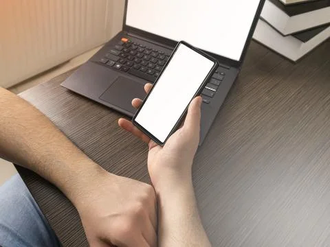 A man at a computer. Close-up of a hand, Mockup. White laptop and phone screen. Stock Photos
