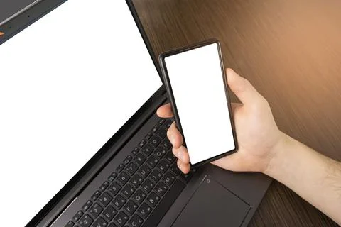 A man at a computer. Close-up of a hand, Mockup. White laptop and phone screen. Stock Photos