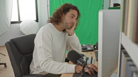 Man at computer with hand on cheek in studio with green screen, microphone,.. Stock Footage 347831474