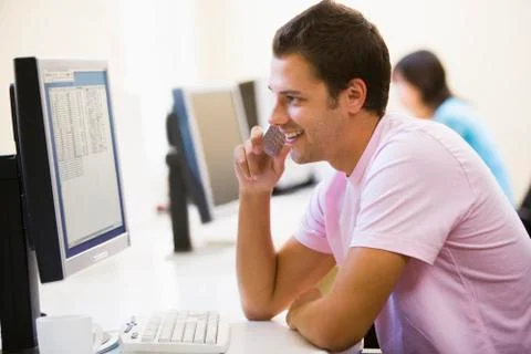 Man in computer room using cellular phone and smiling Foto stock