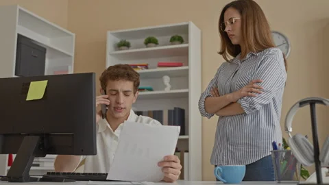 Man at computer talking on phone while woman stands with hand to forehead i.. Stock Footage 339259277