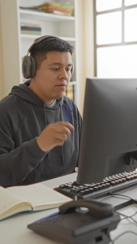 Man at computer wearing headphones writing with pen in a building office de.. Stock Footage 337356086