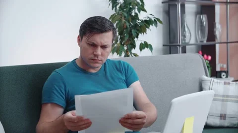 A man is concentrating on documents while sitting on the couch at home. Stock Footage 146539469
