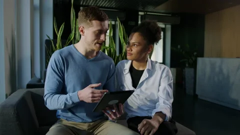A man conducts training on a tablet for his female colleague in office Stock Footage 195204080
