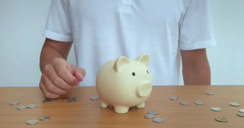 Man confidently puts coin into ceramic piggy bank, preserving savings. Person Stock Footage 270416755