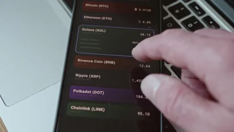 Man confirming cryptocurrency payment on smartphone with laptop in background Stock Footage 337998374