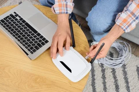 Man connecting an ethernet cable to a white wireless router on a wooden table Stock Photos