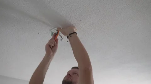 A man connects electrical wires on the ceiling while preparing to install a Stock Footage 316294231