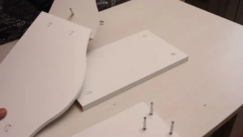 A man connects elements of a table shelf. He pulls them together with eccen.. Stock Footage 255385007