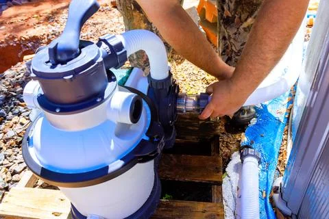 Man connects pool pump to water system at backyard in daylight during summer Stock Photos