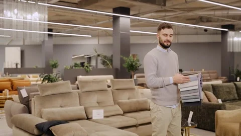 Man considering fabric swatches for sofa upholstery in furniture store showroom Stock Footage 334654197