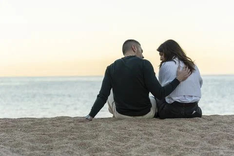 Man consoling her friend while sitting on the sand at the beach Stock Photos