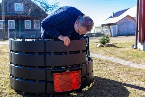 Man constructing compost bin piece by piece from modular plastic parts in yar Фото