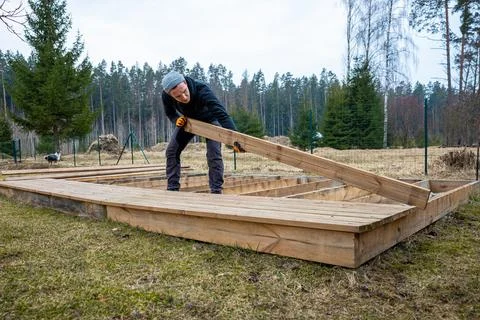Man constructing a wooden deck or terrace in a rural outdoor setting, demon.. Stock Photos