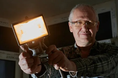 A man at a construction site demonstrates a lantern that he uses to illuminate Stock Photos
