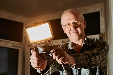 A man at a construction site demonstrates a lantern that he uses to illuminate Stock Photos