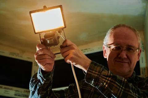 A man at a construction site demonstrates a lantern that he uses to illuminate Stock Photos