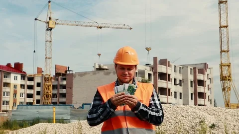 A man in a construction vest and a construction helmet recounts money against Stock Footage 129164148