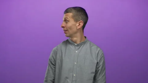 Man with a contemplative expression standing against a vibrant purple backg.. Vidéo 314244435