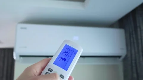 The man is controlling the air conditioner with the remote control in his hand. Stock Footage 315979398
