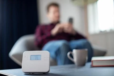 Man Controlling Central Heating Smart Meter Using App On Mobile Phone Stock Photos