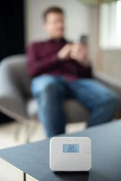 Man Controlling Central Heating Smart Meter Using App On Mobile Phone Foto stock